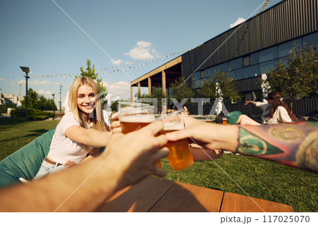 Cheers. Focus on hands and beautiful young girl, friends gathering in public place for summer picnic, enjoying refreshing beer Cheers. Focus on hands and beautiful young girl, friends gathering in public place for summer picnic, enjoying refreshing beer 117025070