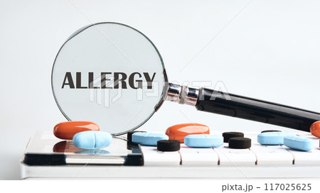 The concept of medicine and health. Spring allergy concept. ALLERGY word written through a magnifying glass on a calculator with tablets on a gray background. The concept of medicine 117025625