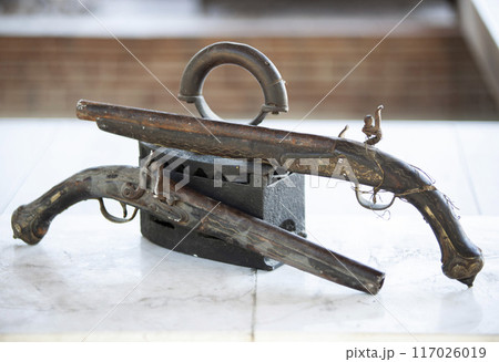 Antique charcoal iron and antique patterned revolvers with forged grips. Antique metalware. Horizontal 117026019