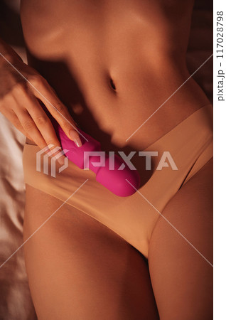 pink vibrator in female hand on stomach of woman girl with a sexy body in panties lying on bed. Sex toys for female satisfaction and orgasm 117028798