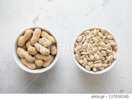 Bowls with whole and peeled healthy peanut nuts on light background. Bowls with whole and peeled healthy peanut nuts on light background. 117030280