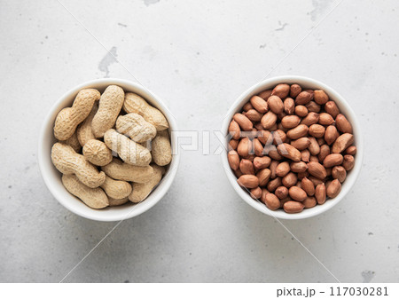 Bowls with whole and peeled healthy peanut nuts on light background. Bowls with whole and peeled healthy peanut nuts on light background. 117030281