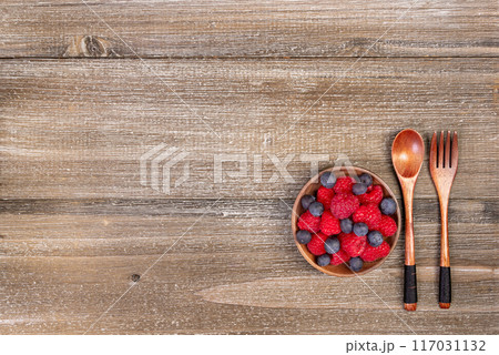 Mix of blueberries and raspberries in a plate with wooden fork and spoon. 117031132