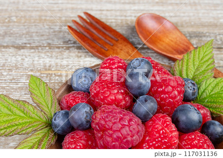Mix of blueberries and raspberries in a plate with wooden fork and spoon. Mix of blueberries and raspberries in a plate with wooden fork and spoon. 117031136