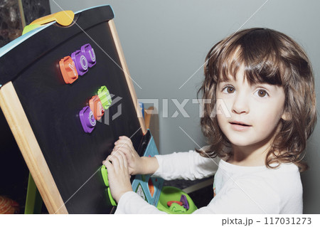 Toddler girl learning letters on the magnetic easel at home. Toddler girl learning letters on the magnetic easel at home. 117031273