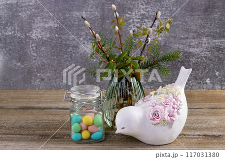 Easter colorful candies, pussywillow and a figurine of bird on the table. Easter colorful candies, pussywillow and a figurine of bird on the table. 117031380