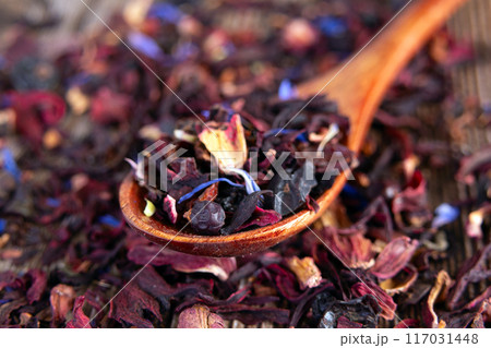 Tea mix of karkade, flowers and berries in a spoon and on the table. Tea mix of karkade, flowers and berries in a spoon and on the table. 117031448