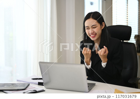 Excited young female worker reading good news on her laptop and celebrating a success 117031679