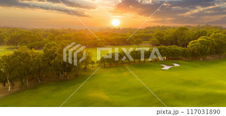 Panorama of golf course at sunset with dramatic sky. Scenic panoramic view of golf fairway with pond. Golf field with beautiful pines 117031890