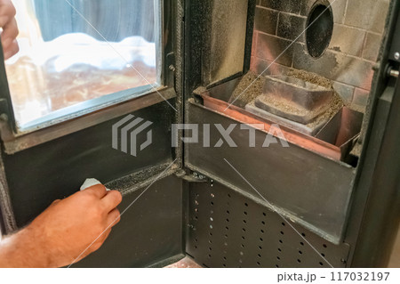 Close-up of a man cleaning the soot produced by the pellet stove in his living room, sustainable heat. Renewable energy. Close-up of a man cleaning the soot produced by the pellet stove in his living room, sustainable heat. Renewable energy. 117032197