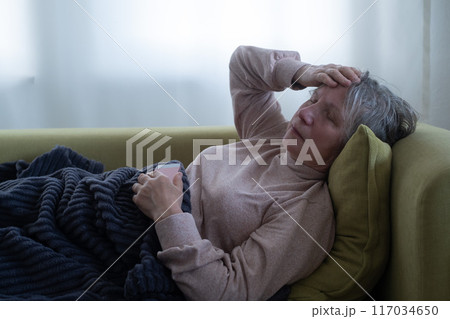 A sick old woman laying down in bed and having migraine. A sick old woman laying down in bed and having migraine. 117034650