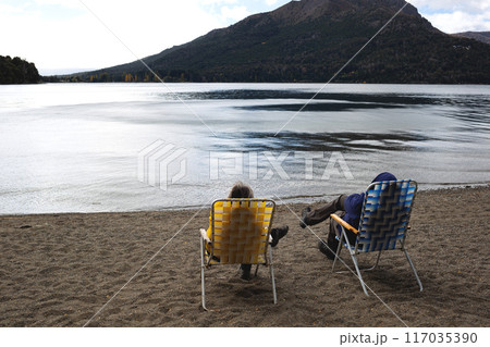 Two people relax on a tranquil lakeside beach, enjoying the scenic mountain view 117035390