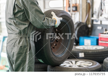 自動車整備工場でタイヤを運ぶ男性メカニック（肉体労働・重労働・重い・腰痛） 117035735