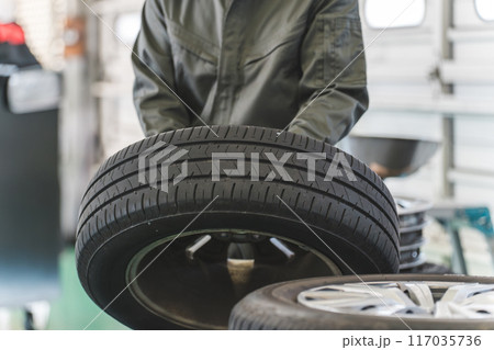 自動車整備工場でタイヤを運ぶ男性メカニック（肉体労働・重労働・重い・腰痛） 117035736