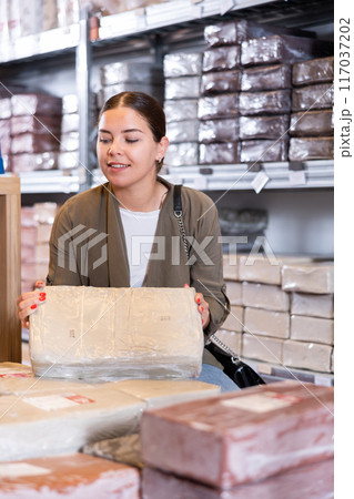 Female customer chooses briquettes with white clay in specialized store 117037202