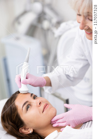 Young woman having face laser therapy procedure by specialist 117037328