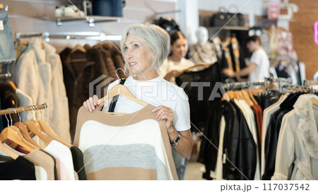 Old woman choosing convenient jumper in clothing store 117037542