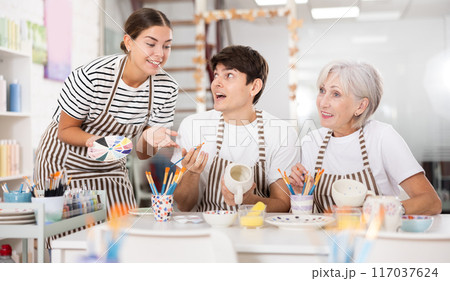 Group of cheerful people painting ceramic dishware in pottery class Group of cheerful people painting ceramic dishware in pottery class 117037624