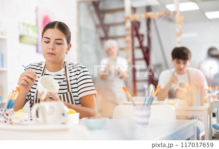 Young female artist painting ceramic cup in pottery workshop Young female artist painting ceramic cup in pottery workshop 117037659