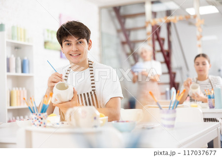 Cheerful skilled young artist painting ceramic cup in pottery workshop Cheerful skilled young artist painting ceramic cup in pottery workshop 117037677