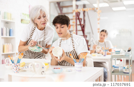 Experienced female ceramicist teaching enthusiastic guy to paint pottery 117037691