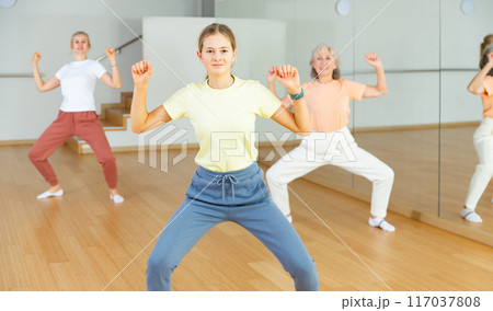 Teen girl with family exercising dance moves with group of people in dance center Teen girl with family exercising dance moves with group of people in dance center 117037808