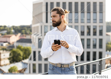 Man in white shirt using smartphone on rooftop with city view 117039701