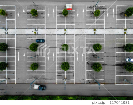 An aerial perspective shows an empty parking lot with a few cars and scattered trees surrounding it 117041081