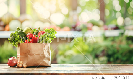 Paper bag with fresh vegetables including lettuce, tomatoes, onions and broccoli on a wooden table with a blurred garden background Paper bag with fresh vegetables including lettuce, tomatoes, onions and broccoli on a wooden table with a blurred garden background 117041516