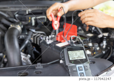 Man is measuring AGM battery power of suv car by battery tester at home. 117042247