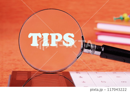 Conceptual tax symbol. Copy space. TIPS word written through a magnifying glass on an orange background 117043222
