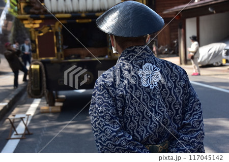 日本の岐阜県高山市　春の高山祭　屋台と呼ばれる豪華な山車　法被を着て陣笠を被っている男性の後ろ姿 117045142