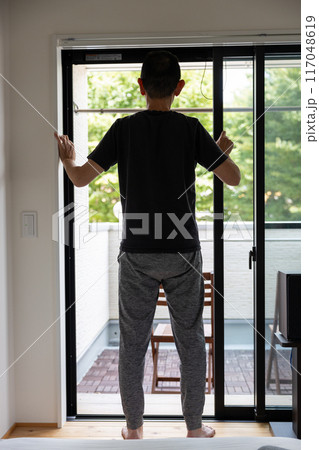 部屋のサッシを開けている男性の後ろ姿 117048619
