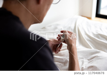 ベッドの上で体温計を見ている男性 117048678