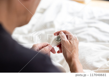 ベッドの上で体温計を見ている男性 117048681