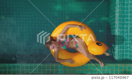 Beautiful woman in bikini relax on bright yellow duck inflatable ring float turquoise swimming pool private villa. Girl relax outdoor lifestyle travel summer holiday vacation. Aerial zoom out Thailand 117048967