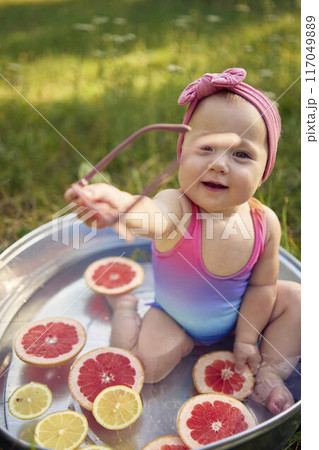 baby wearing sunglasses in a metal bath in a summer garden plays with grapefruit and lemon slices baby wearing sunglasses in a metal bath in a summer garden plays with grapefruit and lemon slices 117049889