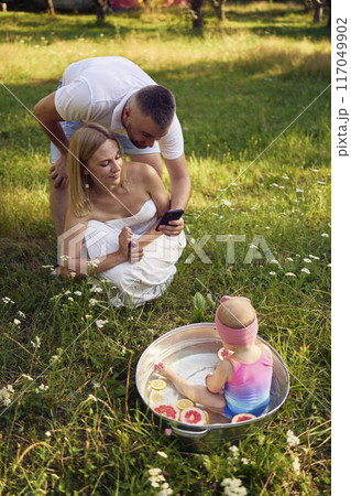mom and dad take smartphone photos of their baby in a metal bath in the summer garden mom and dad take smartphone photos of their baby in a metal bath in the summer garden 117049902