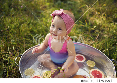 a baby in a metal bath in a summer garden plays with grapefruit and lemon slices 117049911