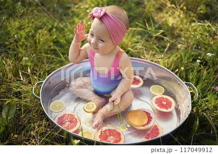 a baby in a metal bath in a summer garden plays with grapefruit and lemon slices 117049912