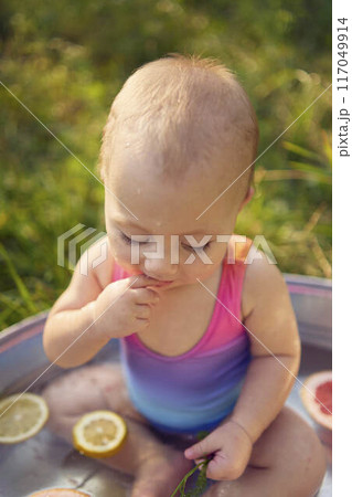 a baby in a metal bath in a summer garden plays with grapefruit and lemon slices 117049914