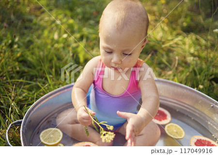 a baby in a metal bath in a summer garden plays with grapefruit and lemon slices 117049916