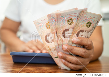 Asian business woman holding Thai banknote currency money and counting with calculator. Asian business woman holding Thai banknote currency money and counting with calculator. 117050087