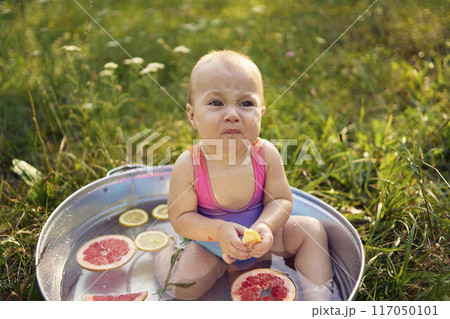 a baby in a metal bath in a summer garden plays with grapefruit and lemon slices 117050101