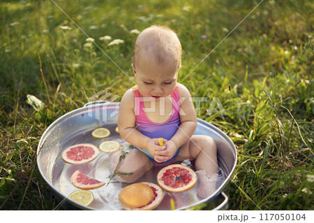 a baby in a metal bath in a summer garden plays with grapefruit and lemon slices a baby in a metal bath in a summer garden plays with grapefruit and lemon slices 117050104