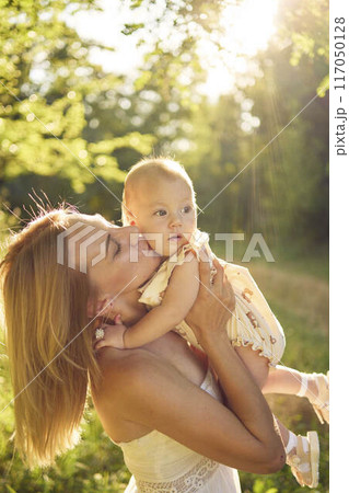 a mother plays with her baby daughter in a sunlit garden a mother plays with her baby daughter in a sunlit garden 117050128
