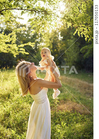 a mother plays with her baby daughter in a sunlit garden 117050133