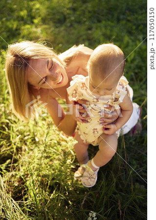 a mother plays with her baby daughter in a sunlit garden a mother plays with her baby daughter in a sunlit garden 117050150