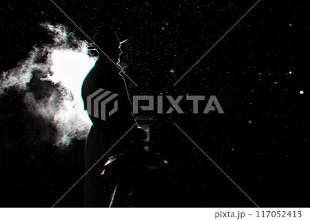 dramatic silhouette of a dangerous man in a hat at night in the rain in the city 117052413