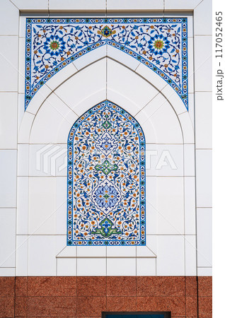 ceramic tile with a traditional Uzbek floral ornament with a oriental pattern. Wall of white islamic mosque Minor in Uzbekistan 117052465